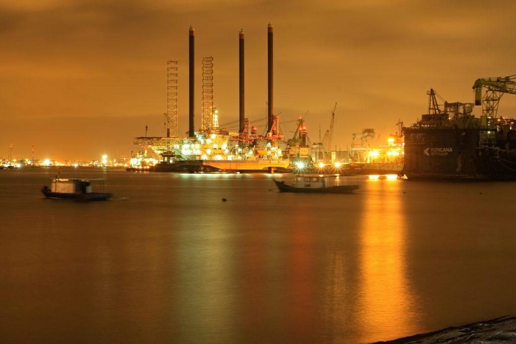 Oil refinery illuminated at night, illustrating the September 2026 energy shock affecting inflation, bond yields and Bitcoin